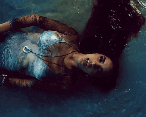 a woman is laying in the water with her hand reaching out