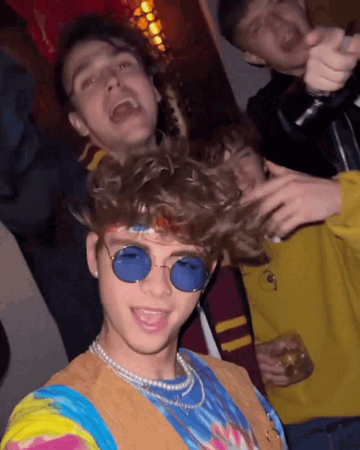 a man wearing blue sunglasses and a pearl necklace poses for a photo