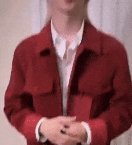 a man wearing a red jacket and a white shirt is standing with his hands folded .