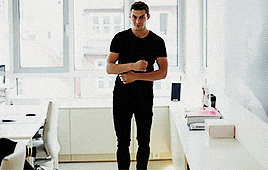 a man in a black shirt is standing in front of a window in an office