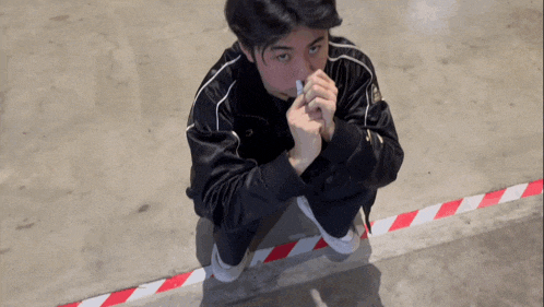 a man in a black jacket is kneeling down with his hands folded in front of his face