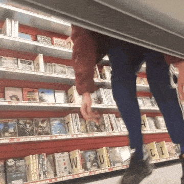 a person is standing under a shelf in a book store looking at books .