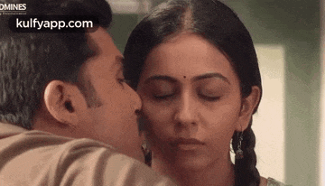 a man is kissing a woman on the forehead with his eyes closed .