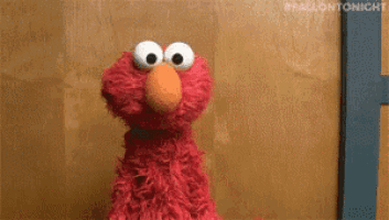 elmo from sesame street is standing in front of a door and looking at the camera .