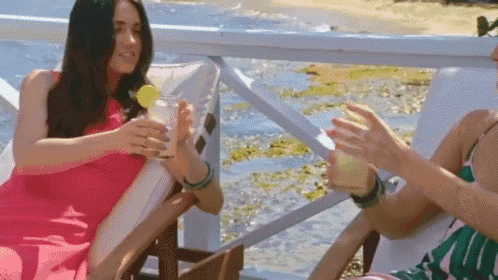 two women are sitting in chairs drinking cocktails on a pier .