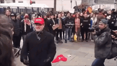 a man wearing a red maga hat stands in front of a crowd of people