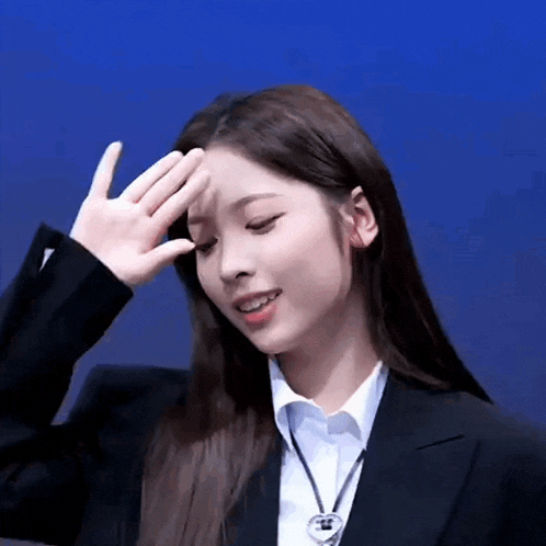 a woman in a suit is holding her hand to her forehead .