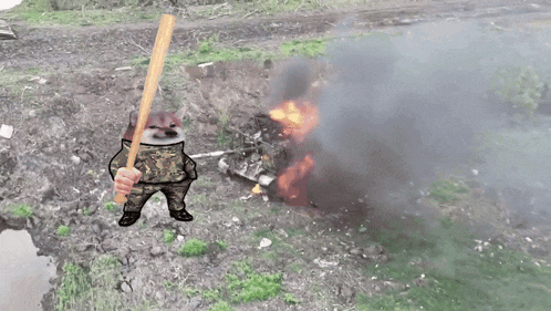 a cat in a military uniform is holding a baseball bat in front of a burning vehicle