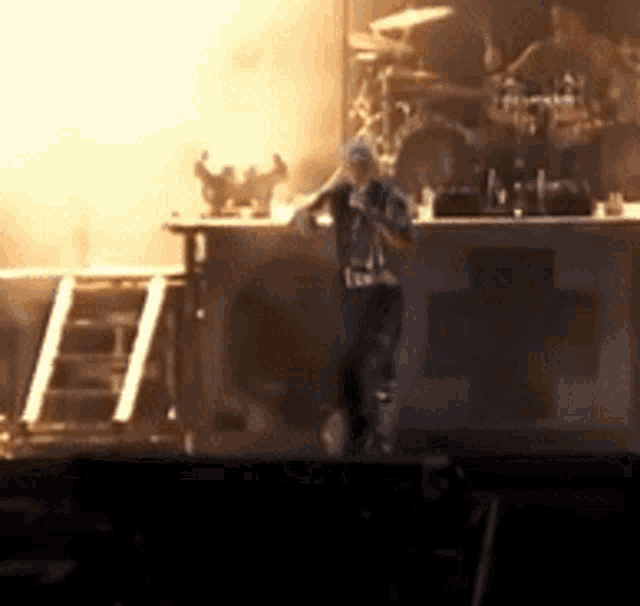 a blurred image of a man on a stage with the letter h in the corner