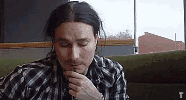 a man with long black hair is sitting on a green couch .