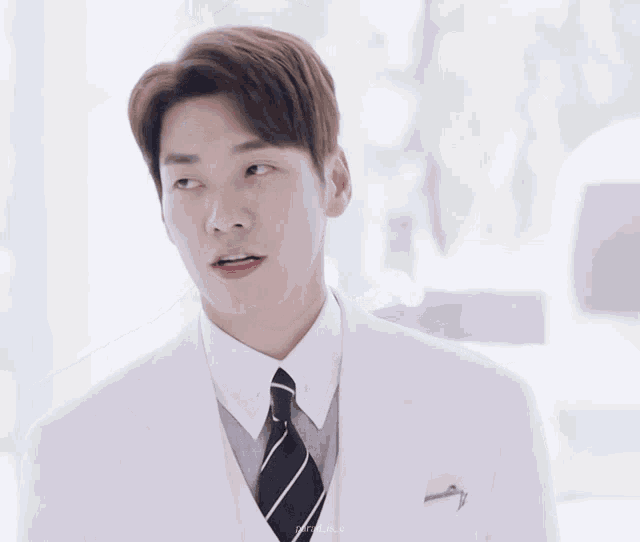 a man in a white suit with a black striped tie is smiling