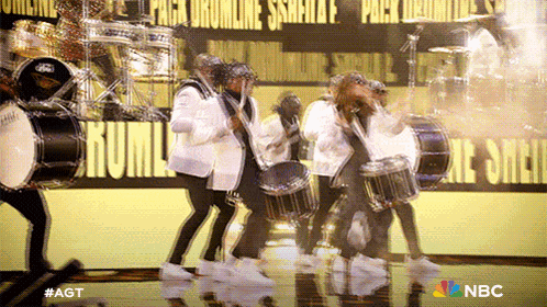 a group of people playing drums on a stage with a nbc logo in the background