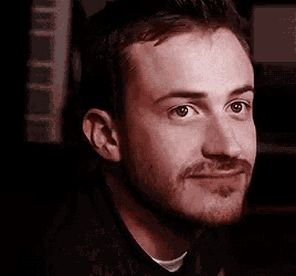 a close up of a man 's face with a beard wearing a black shirt