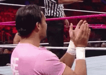 a wrestler in a pink shirt is clapping in a wrestling ring .