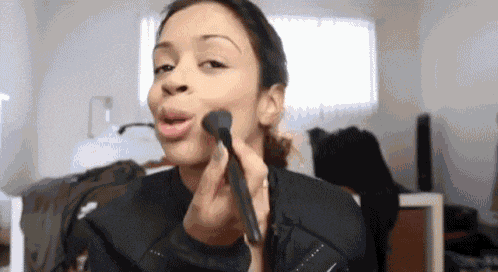 a woman is applying makeup on her face with a brush .