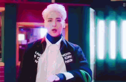 a man with white hair and a black jacket is standing in a dark room .