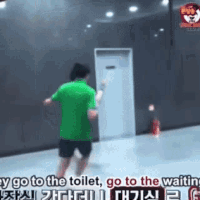 a man in a green shirt and black shorts is standing in front of a door .