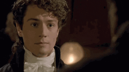 a young man with curly hair and a bow tie is looking at another man .