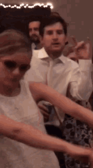 a group of people are dancing at a wedding reception while a man looks on .