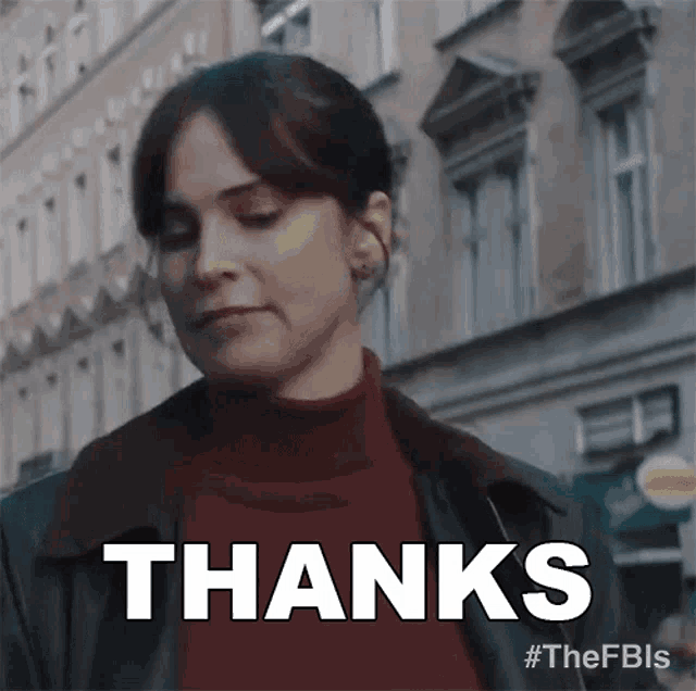 a woman is standing in front of a building and giving a thanks sign .