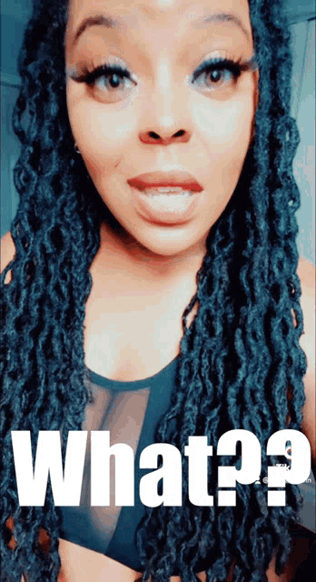 a woman with dreadlocks is wearing a black top with the words what ? on it