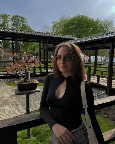 a woman wearing sunglasses and a black shirt stands in front of a bonsai tree
