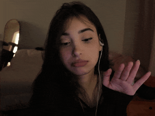 a woman wearing ear buds and a black shirt shows her middle finger