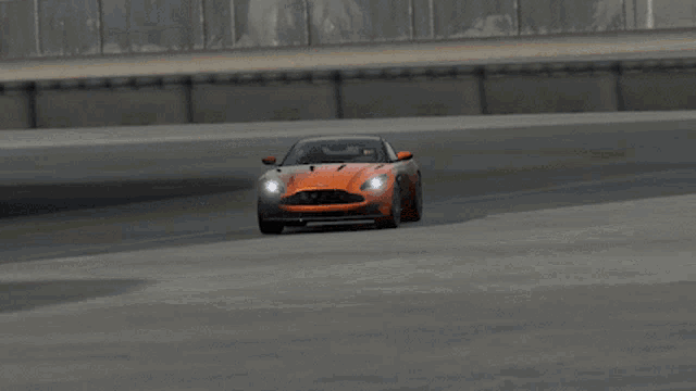an orange aston martin sports car is driving on a track