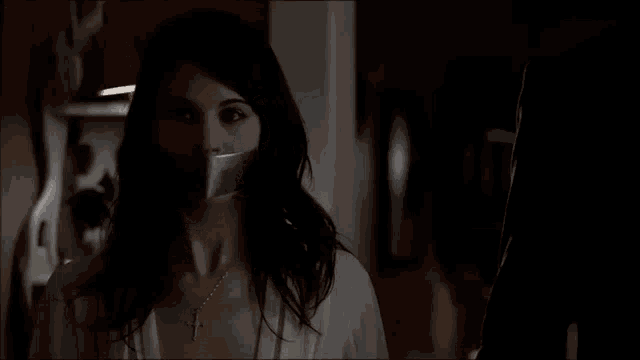 a woman with duct tape on her mouth is looking out a window in a dark room .