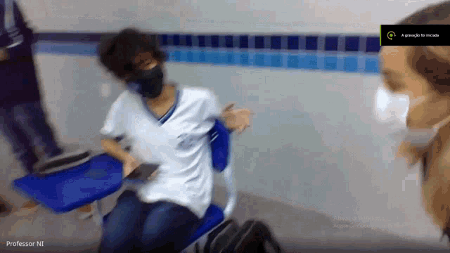 a person wearing a mask is sitting at a desk in front of a professor n.