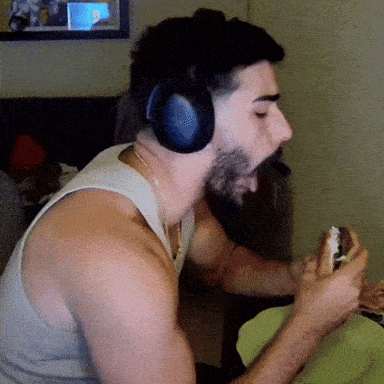 a man wearing headphones and a tank top eating a sandwich