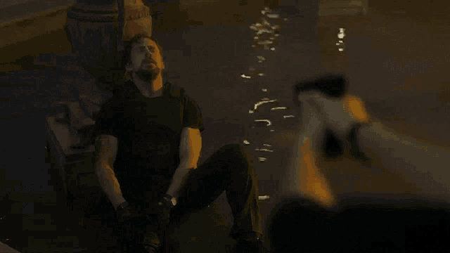 a man in a black shirt is kneeling down with a gun in his hand