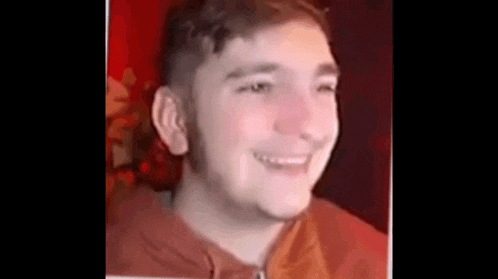 a young man with a beard is smiling in a red shirt .