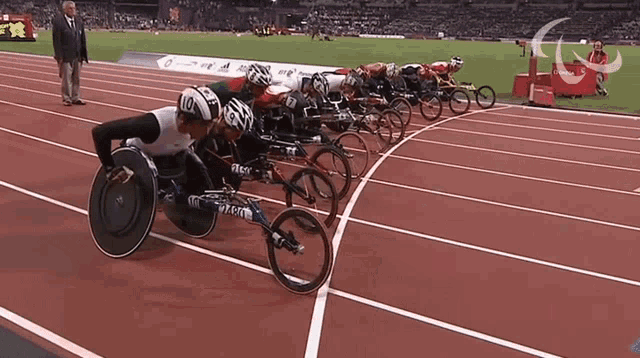 a group of wheelchair racers are lined up on a track and one of them has the number 10 on his helmet
