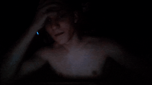 a shirtless man is talking on a phone in the dark