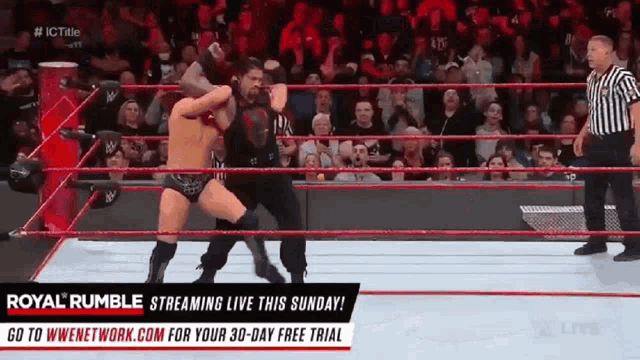 two men are wrestling in a ring with a referee in front of a crowd .