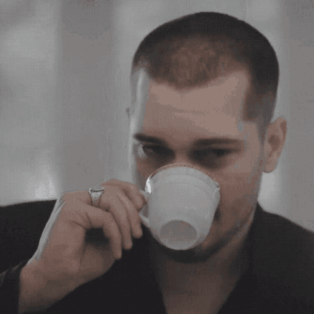 a man wearing a ring is drinking from a white cup