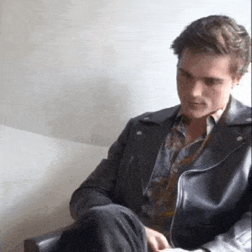 a man is sitting in a chair wearing a leather jacket and a floral shirt .