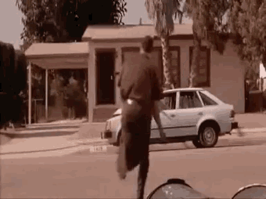 a man is running towards a white car on the side of the road .