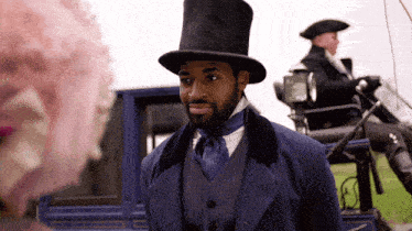 a man wearing a top hat is standing in front of a blue carriage