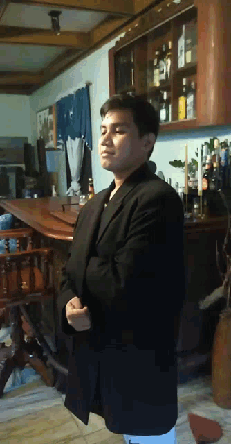 a man in a black suit stands in front of a shelf full of bottles