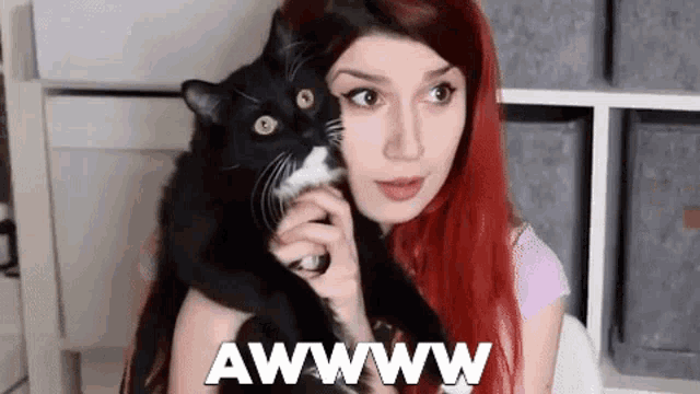 a woman with red hair is holding a black and white cat in her lap .