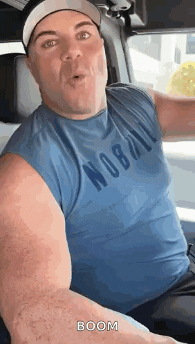 a man in a blue tank top is sitting in a car .