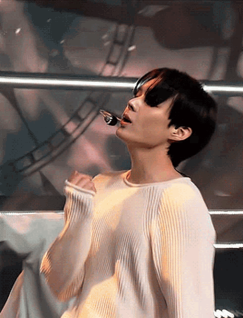 a young man is singing into a microphone while wearing a white sweater
