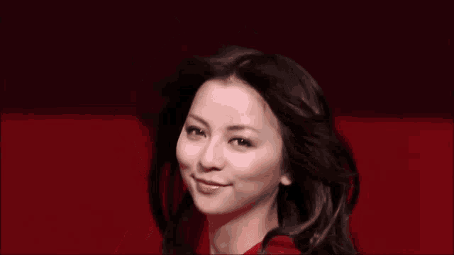 a woman in a red dress is smiling and her hair is blowing in the wind