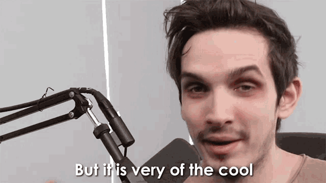 a man speaking into a microphone with the words but it is very of the cool behind him