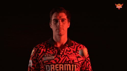 a man in a red shirt stands in front of a black background with a crown on it