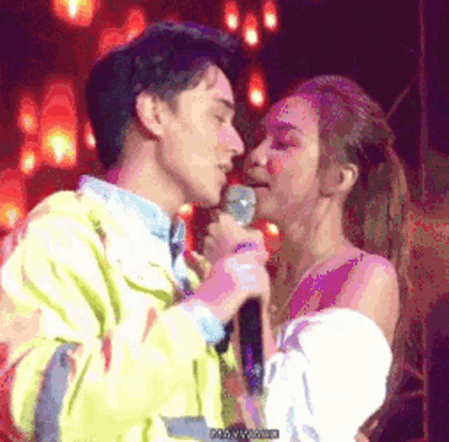 a man and a woman are kissing in front of a microphone .