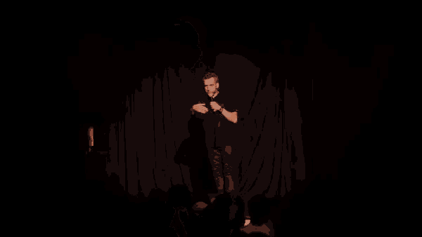 a man in a black shirt is standing on a stage holding a microphone in his hand .
