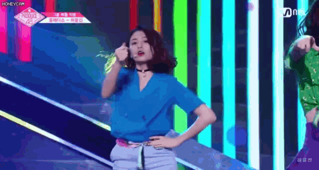 a woman in a blue shirt is standing on a stage in front of a colorful background .